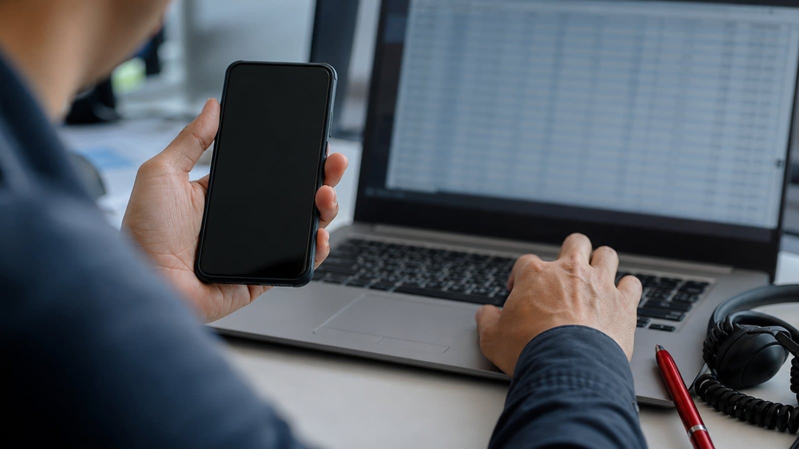 Hands at a desk with a smartphone, a laptop and a headset