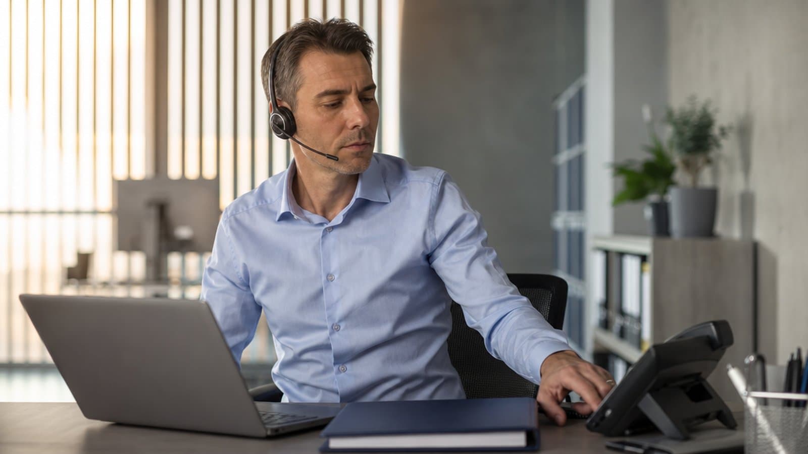A compliance professional at a desk with a headset and a desk phone